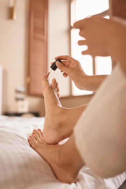 Aplicación de esmalte terracota en las uñas de los pies, con luz cálida.