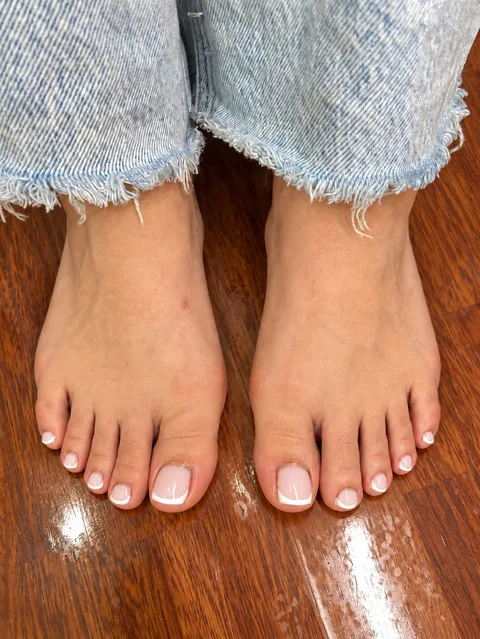 Pedicura francesa con base rosa clara, pies descalzos y vaqueros desflecados.