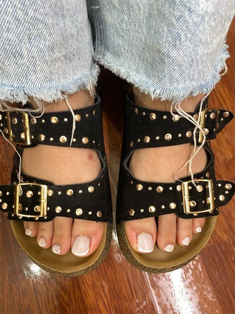 Pedicura francesa con base rosa clara, sandalias negras con hebillas y vaqueros desflecados.