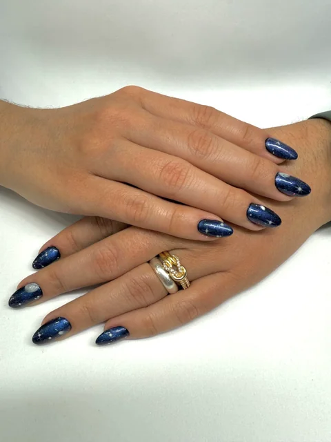 Uñas almendradas azul noche con destellos plateados.